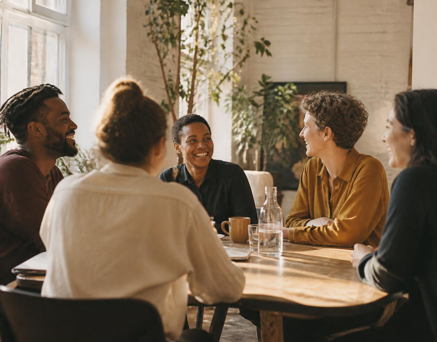 A small group of professionals talking and laughing around a sunlit table